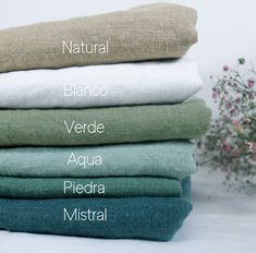 four different colors of linens stacked on top of each other with flowers in the background