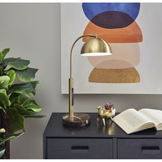 an open book sitting on top of a table next to a lamp and potted plant