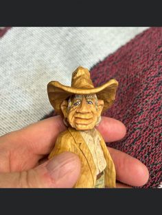 a hand holding a small wooden toy with a cowboy hat on it's head