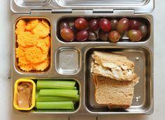 a lunch box with grapes, celery, crackers and bread in it