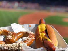 two hotdogs with mustard and ketchup are in a paper container on a baseball field