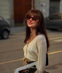 a young woman is walking down the street with her hand in her pocket and wearing sunglasses