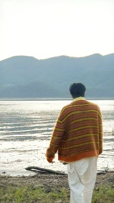 a man standing on top of a grass covered field next to the ocean with mountains in the background