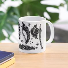 a white coffee mug sitting on top of a wooden table next to a book and plant