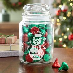 a glass jar filled with holiday treats next to a christmas tree