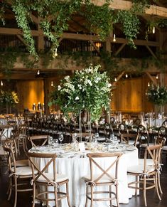 the tables are set up with white linens and greenery hanging from the ceiling