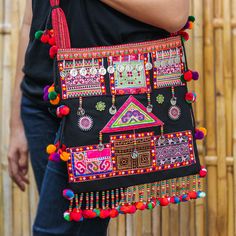 The beauty of the Hmong arts inspires a glorious shoulder bag made in their people's honor. Featuring traditional details made by hand, this colorful accessory with a black base hue is presented by Thai artisan Kunlaya Pangsiri, who adds embroidered details and pompoms to her design. On top of that, the piece has little leaf boxwood, aluminum and plastic beads for a unique touch and comes equipped with two interior pockets and a zipper closure. Cheap Multicolor Traditional Shoulder Bag, Hmong Food, Hmong Fashion, Hmong Embroidery, Hmong Clothes, Afghan Clothes, Colorful Accessories, Denim Diy, Boutique Dress Designs