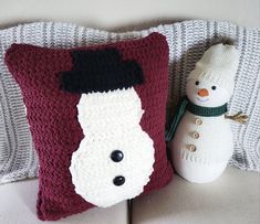 a crocheted snowman pillow sitting next to a stuffed snowman on a couch