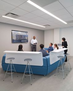 several people are sitting on a blue couch in an office with a projector screen