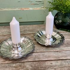 two white candles sitting on top of metal plates