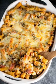 a casserole dish filled with pasta and cheese, topped with a wooden spoon