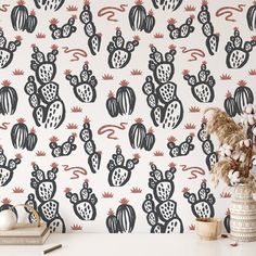 a white table topped with a vase filled with flowers next to a wallpaper covered in black and red cacti