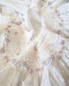 a white dress with pink flowers on it and a sewing needle in the middle of the skirt