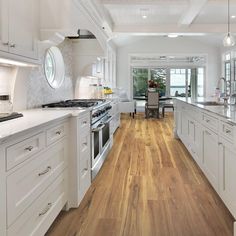 a large kitchen with white cabinets and wood flooring, along with a dining room table