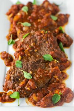 meat with tomato sauce and basil leaves on a white platter, ready to be eaten