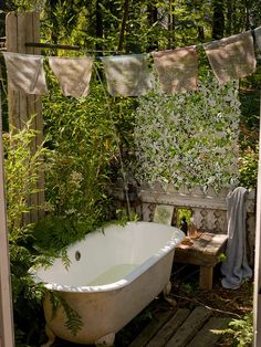 an old bathtub in the middle of a garden with clothes hanging from it's sides