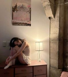 a woman sitting on top of a dresser next to a lamp