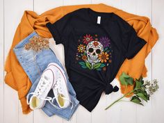 Celebrate the season in style with our Día de los Muertos shirt! Featuring a beautiful floral skull design, this fall Halloween shirt honors the vibrant traditions of Día de Muertos. Whether you're looking for a Latina skeleton shirt or a stylish skull t-shirt, these designs bring culture and beauty to your autumn wardrobe. Perfect for honoring the holiday while staying fashionable! STYLE + SIZING ★ UNISEX Bella+Canvas 3001 T-Shirt ★ Colors may vary (see photo card for more info). ★ See photos f Multicolor Skull Print Tops For Halloween, Black Graphic Print Top For Day Of The Dead, Halloween Multicolor Skull Print Tops, Casual Skull T-shirt For Fall, Cotton Graphic Print Top For Day Of The Dead, Day Of The Dead Skull Print Short Sleeve Tops, Black Crew Neck T-shirt For Day Of The Dead, Black Short Sleeve T-shirt For Day Of The Dead, Casual Skull Print T-shirt For Halloween