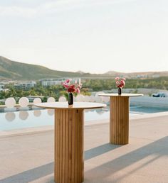 two vases with flowers sit on top of wooden pedestals next to a pool