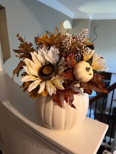 a white pumpkin filled with lots of flowers sitting on top of a table next to a stair case