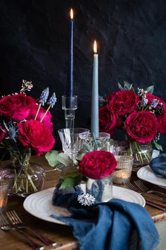 the table is set with candles, plates and flowers in vases on top of it