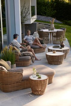 two people are sitting on wicker chairs and tables outside the house with their laptops