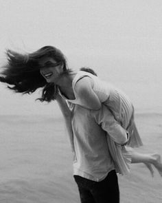 black and white photograph of a woman carrying a man on her back by the ocean