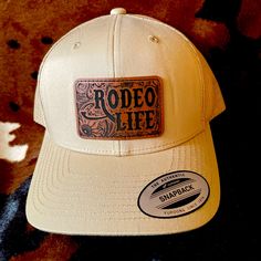 Tan “Rodeo Life” Leather Patch Cap! * 65% Polyester, 35% Cotton *6-Panel, Structured, Hard Buckram Backed Front Panels * Matching Undervisor (Camo And Multicam Have Black Undervisor) * Matching Snapback Closure * 3 1/2" Mid-Profile Crown * 8-Row Stitching On Visor * Permacurv Visor * Measurements (In Inches) One Size Hat Band 24 Crown Height 3 ½ * Adult Unisex Retro Trucker Cap Leather Patch Ideas, Olive Green Hat, Balenciaga Hat, Prada Hat, Diy Hats, Hat Bar, Cattle Brands, Branded Caps, Rodeo Life