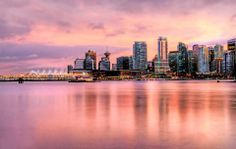 the city skyline is reflected in the water at dusk, with pink and purple hues