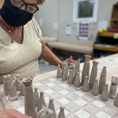 a woman wearing a face mask is making clay chess pieces on a table in a workshop