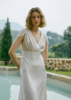 a woman standing in front of a pool wearing a white dress