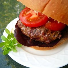 a hamburger with tomato and lettuce on a white plate next to a green leafy plant