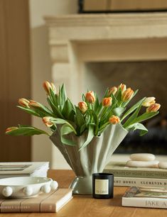 there is a vase with orange flowers on the table next to books and an alarm clock