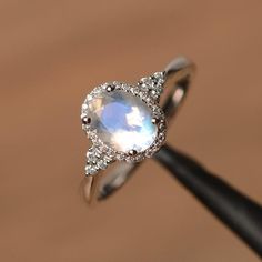 a diamond ring with an oval shaped rainbow colored stone surrounded by small white and clear diamonds