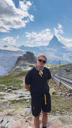 a man standing on the side of a road wearing shorts and a black shirt with yellow stripes