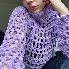 a woman wearing a purple crochet sweater and holding her hand to her ear