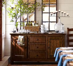 a dining room table with blue chairs and white plates on top of it, in front of two large mirrors