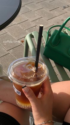 a woman is holding a cup of iced coffee in her hand while sitting at an outdoor table