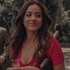 a woman in a pink shirt holding a glass of wine and looking at the camera