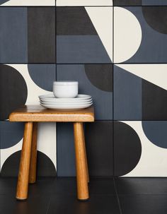 a wooden table with plates and cups on it in front of a wall that has geometric tiles