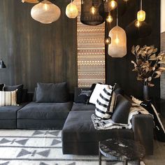 a living room filled with black furniture and hanging lights