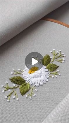 a white flower with green leaves is on the side of a piece of fabric that has been embroidered onto it