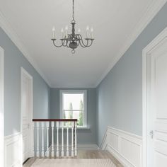 an empty hallway with chandelier and white trim on the walls, painted in blue