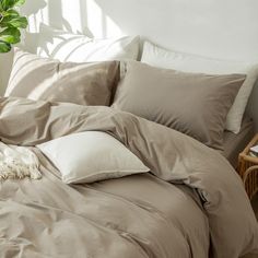 an unmade bed with pillows and blankets on the floor next to a potted plant