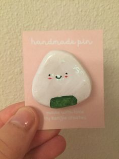 a hand holding a white broccoli pin with a green leaf on it's side