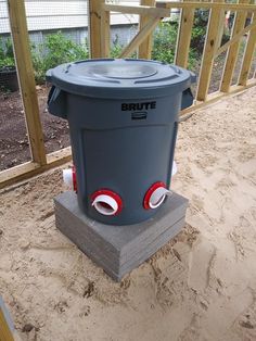 a large gray trash can sitting on top of a cement block next to a wooden fence