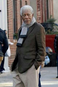 an older man is walking down the street with his hands in his pockets and wearing a scarf around his neck