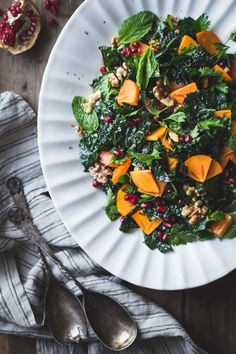 a white plate topped with spinach salad next to two silver spoons and a napkin