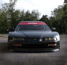 the front end of a black sports car parked in a parking lot next to trees