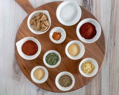 several bowls with different types of spices in them on a wooden plate next to a spoon